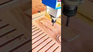CNC milling machine cutting wooden workpiece with spindle bit on slotted bed, wood shavings scattere