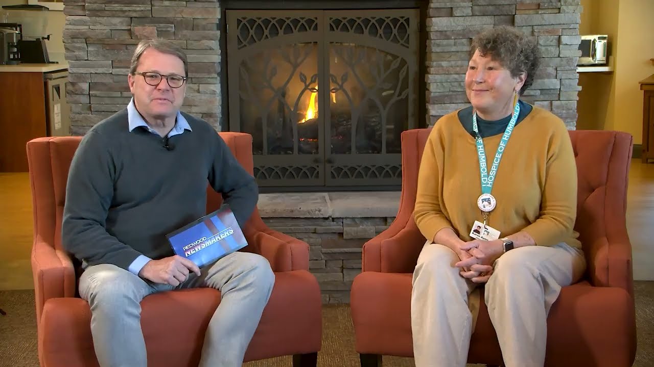 A man and woman sit before a fireplace for an interview.