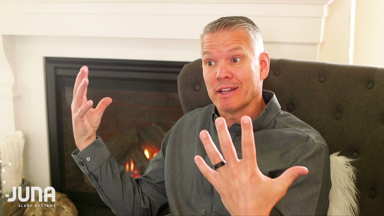 Man discussing the importance of sleep and rest for well-being, in a cozy setting with a fireplace, representing Juna Sleep Systems' focus on customer experience and comfort.