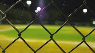 Close-up of fence with blurred baseball field in background