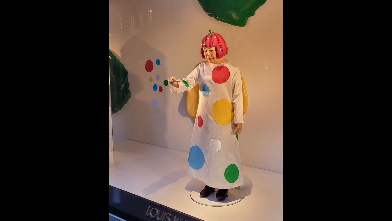 People use their smartphones to take pictures of the Yayoi Kusama robot  painting spots on the window of the luxury retailer Louis Vuitton's Fifth  Avenue store, New York, NY, January 9, 2023.