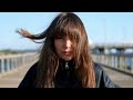 Hot Brunette Woman With Long Hair and Fringe Wearing a Windbreaker Coat Waits in Very Strong Winds