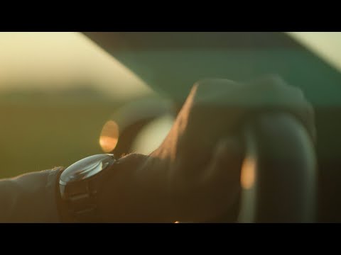 Driver with silver wrist watch turning steering wheel in sunset
