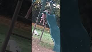 Little girl struggles to climb ladder of slide then falls on the ground in backyard