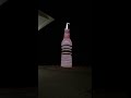 Pops giant soda bottle at night