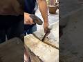 chiseling the surface of the large wooden block using a hammer and metal chisel