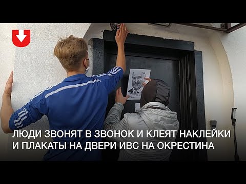Люди звонят в звонок и клеят наклейки и плакаты на двери ИВС на Окрестина