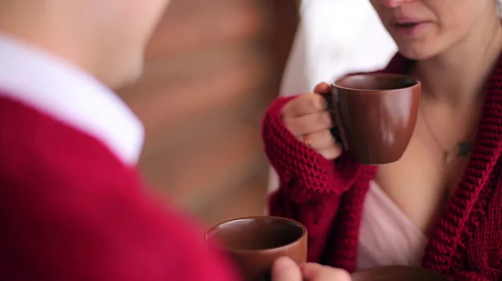 groom and bride drink coffee or tea out of cups on a balcony of wooden log chalet cottag