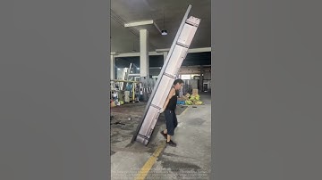 Two workers collaborate to carry heavy door frames in the door frame production workshop.