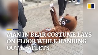 Man in bear costume lays on floor while handing out leaflets in China