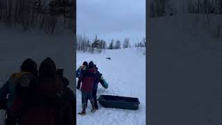 Guy goes downhill on sled then crashes into girl and woman holding baby