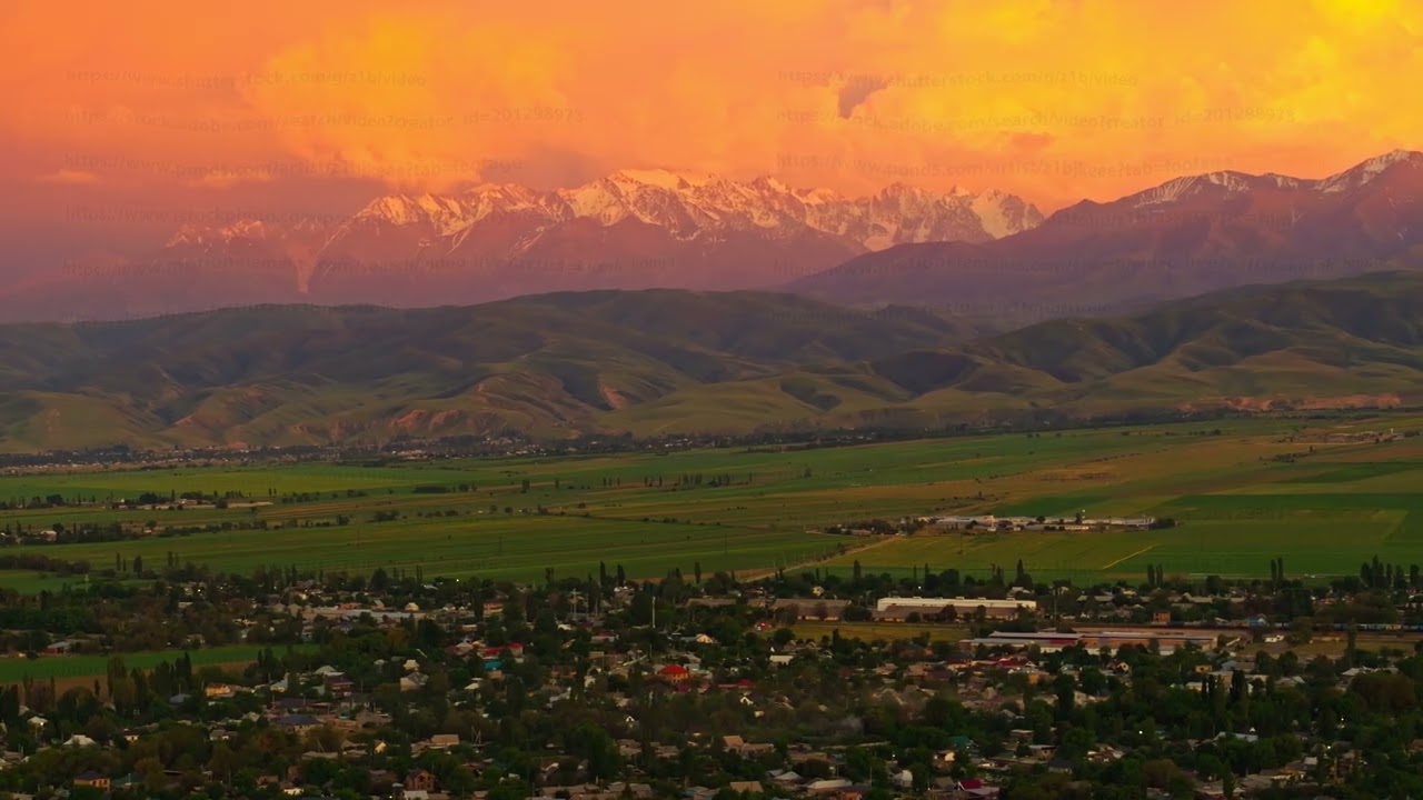 Dramatic sunset over snow-capped mountains and rural landscape in Kyrgyzstan, drone view.