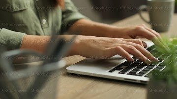 Close up video of female hands typing on laptop keyboard on a modern wooden table. Fingers tapping