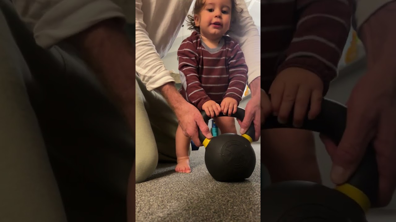 Guy and his son play with kettlebell then boy falls forward and faceplants on carpeted floor