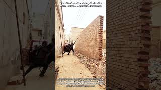Two Workers Use Long Poles To Push Down A Massive Brick Wall