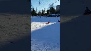Kid goes sledding down hill and crashes into another kid