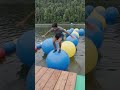 4K photorealistic vlog-style video of me leaping across blue and yellow inflatable balls on a lake