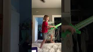 Boy holding green toy sword does ninja warrior stance/pose then fall off bed