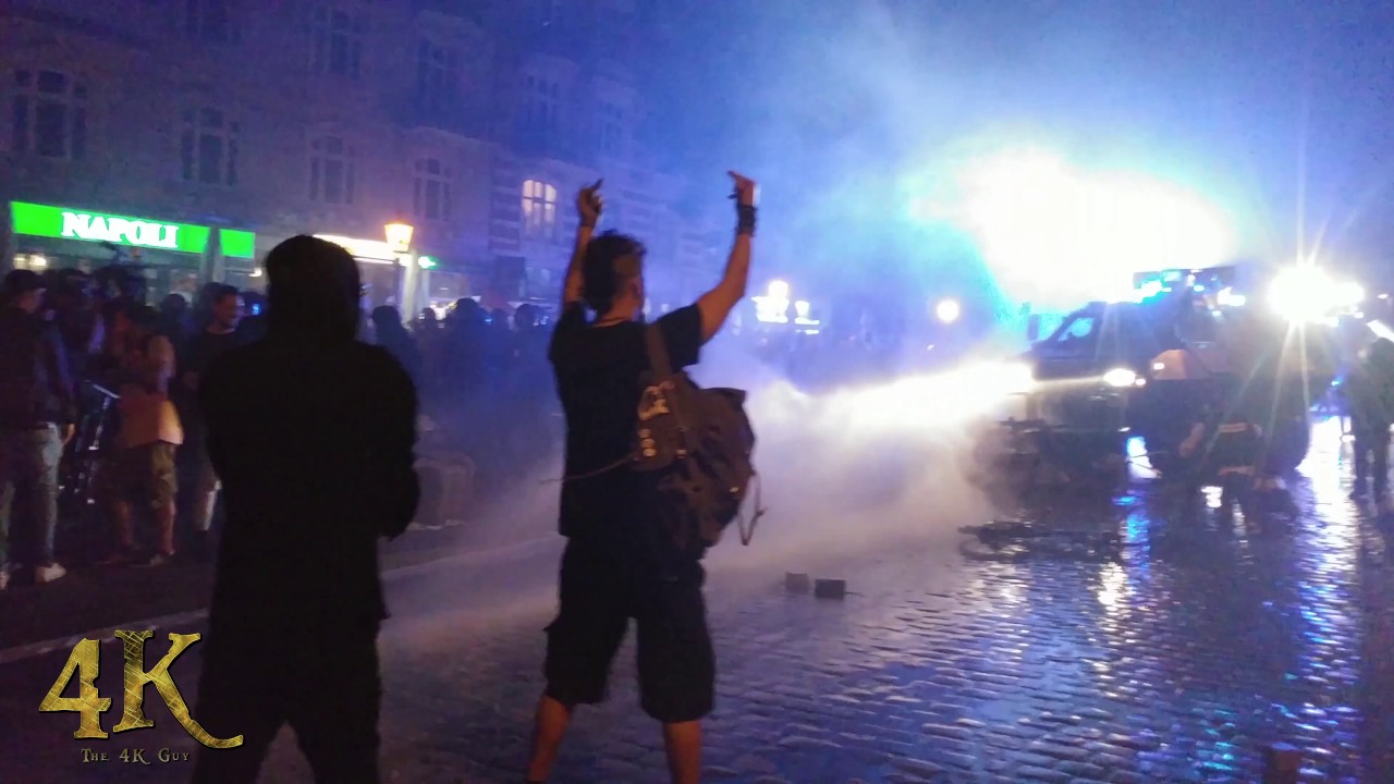 Water cannon spraying camera in chaotic riot at night with angry people