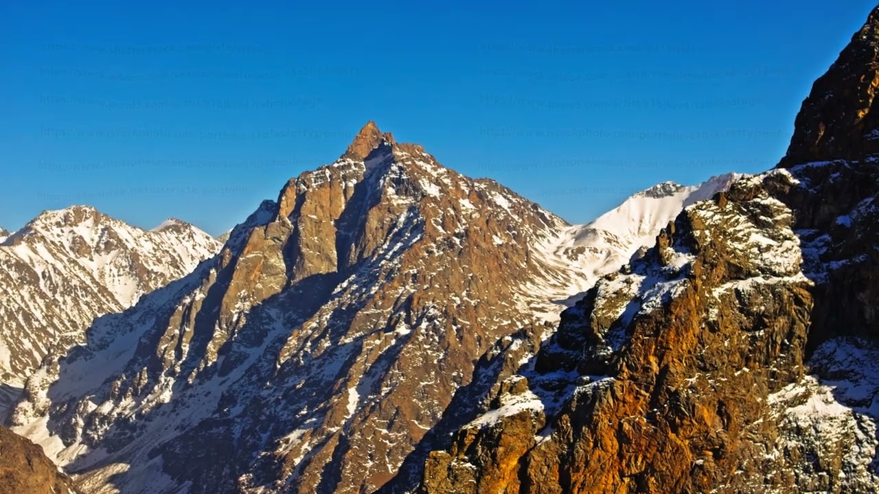 Majestic snow-covered mountains under clear daytime sky, drone view