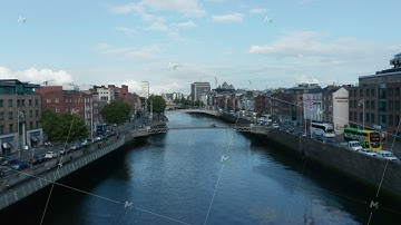 Forwards fly above Liffey bridge. Traffic on bridges and waterfronts. Buildings along river. Dublin