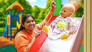 The baby doll goes for a walk and slides down a slide at the playground.