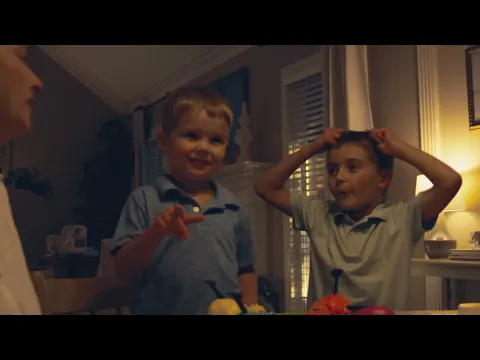 Two young boys in collared shirts laugh together at a table in a softly lit home.