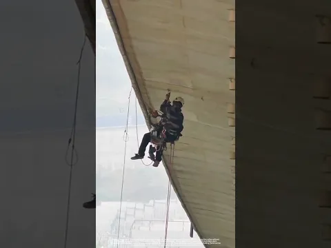 Rope‑access workers install drain pipes under bridge box girder