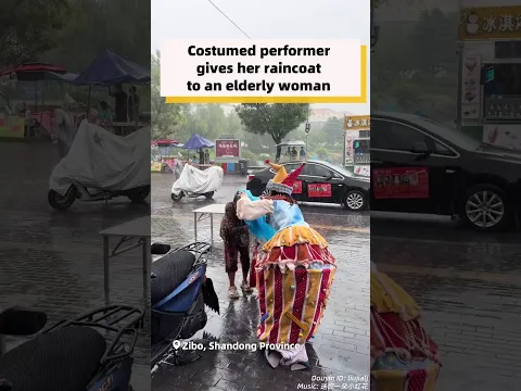 Costumed performer gives her raincoat to an elderly woman