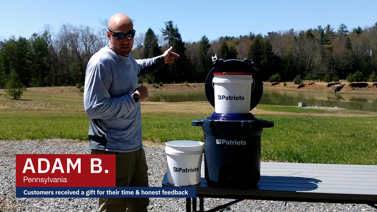 A man identified as Adam B. from Pennsylvania stands outdoors beside a table holding the 4Patriots Outdoor Filtration System. He gestures toward a scenic pond in the background while presenting a video testimonial. 