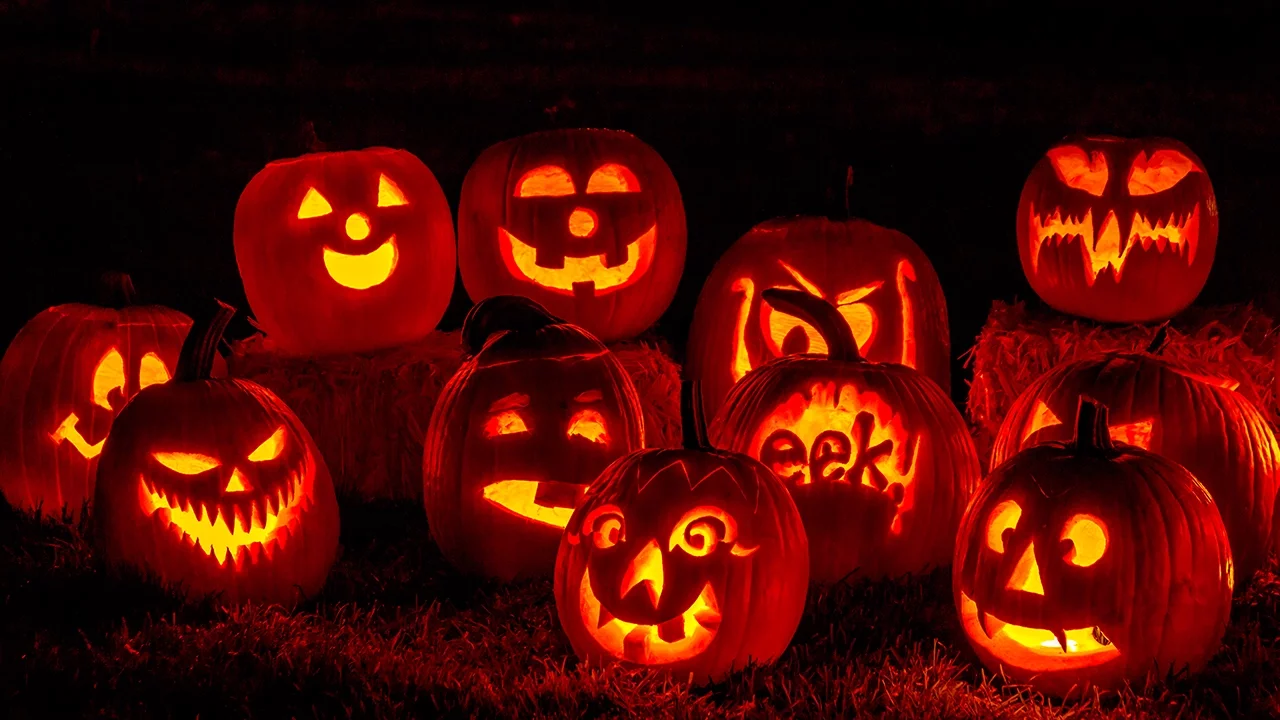 A heap of glowing carved jack-o'-lanterns in the dark, one carved with the word eek