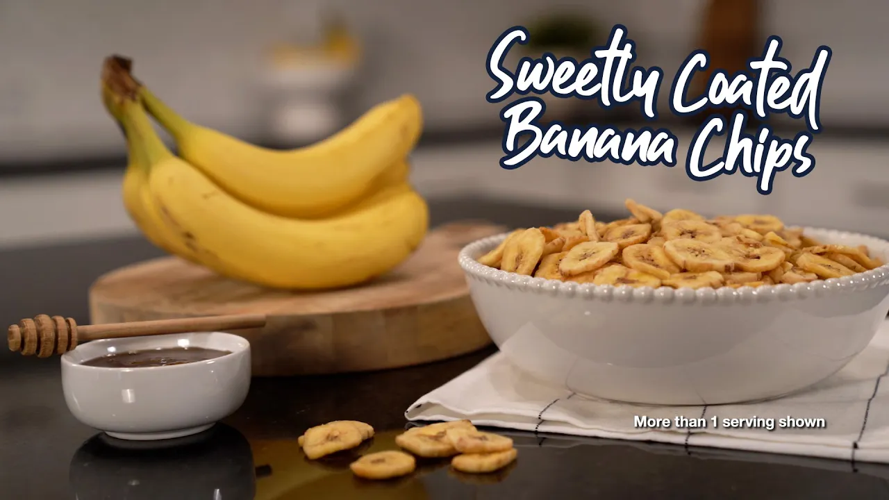 A bowl of sweetly coated banana chips from an emergency survival food kit, shown on a kitchen counter with fresh bananas, honey, and a napkin, highlighting the long-term storage snack option.