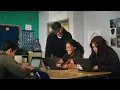 A YouTube thumbnail shows four people looking at laptop screens in a classroom. There is a red YouTube play button in the center of the thumbnail.