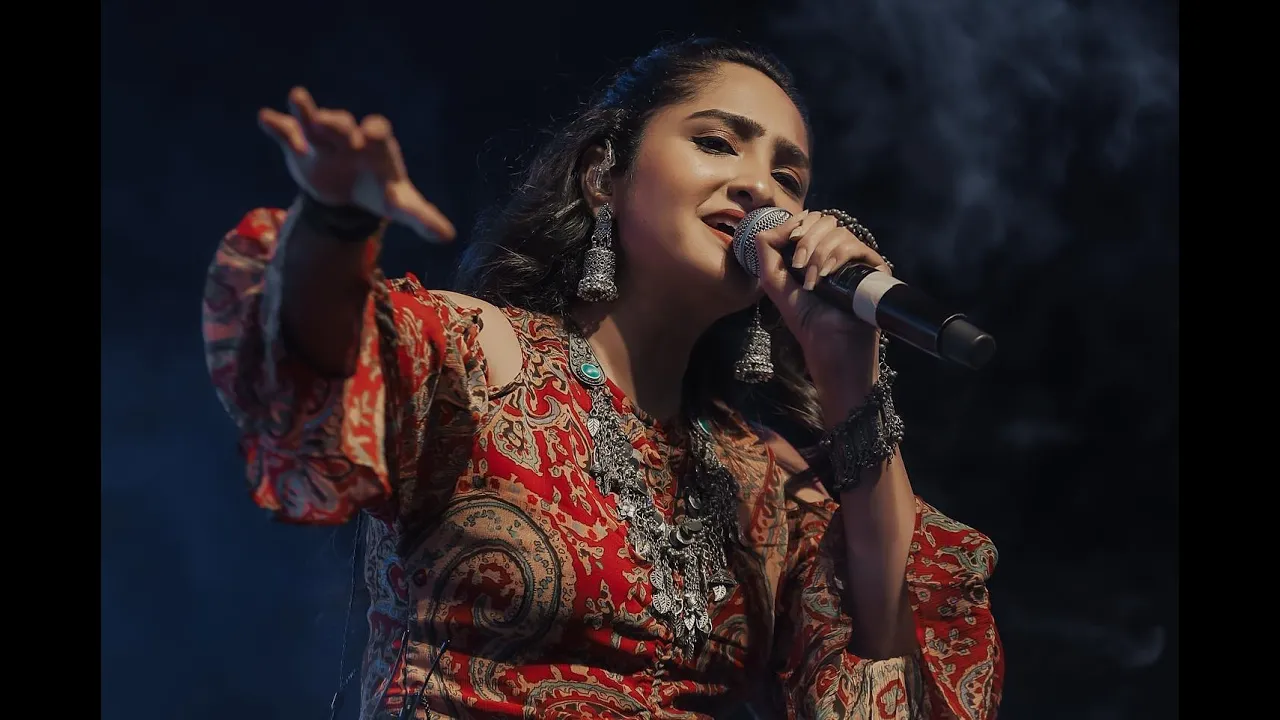 Santvani Trivedi singing into a microphone on stage in a red printed outfit. Still from her 2022 showreel on her YouTube channel.