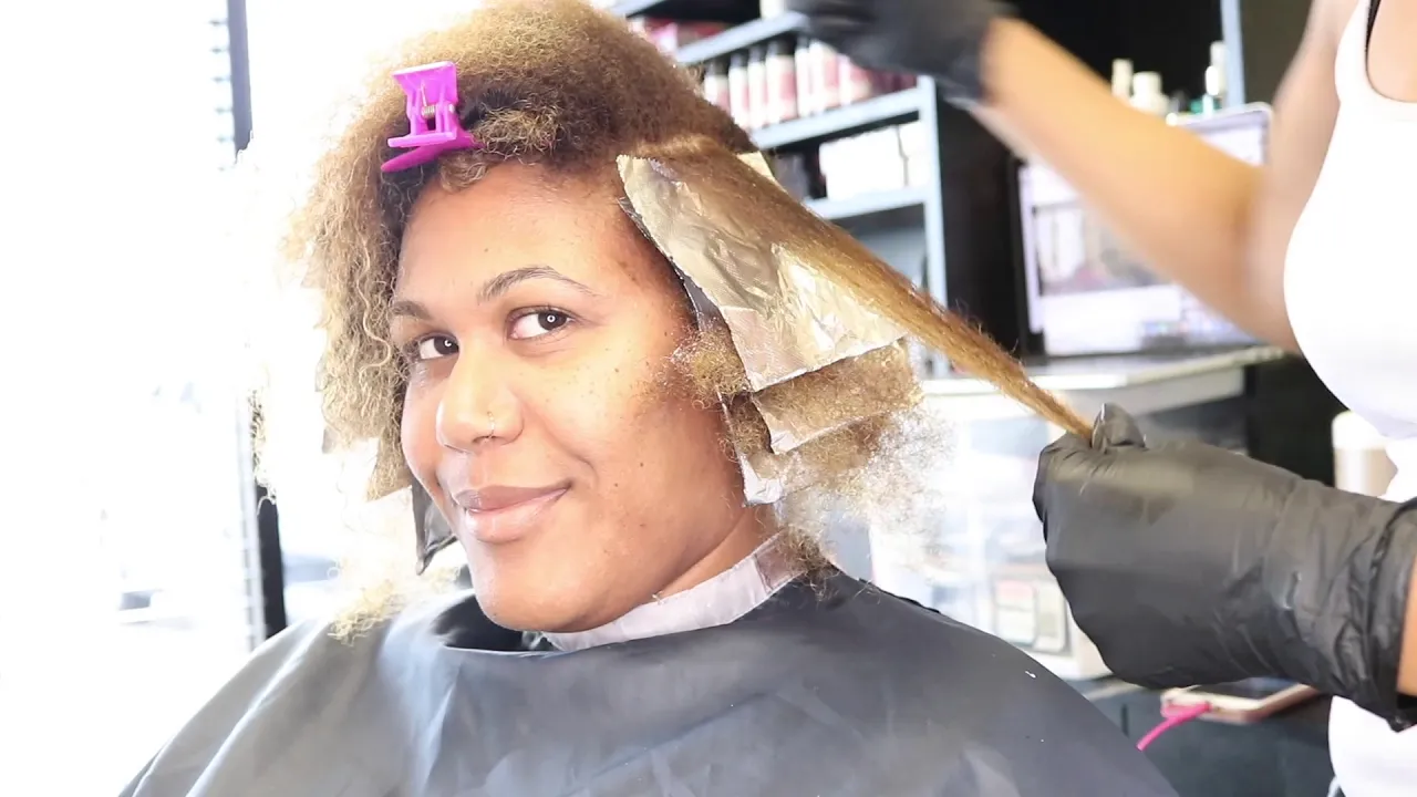 a hairstylist doing a same-day session of hair dyeing and smoothing treatment on a woman with afro hair