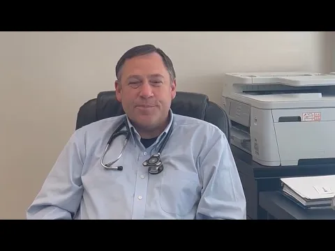 Dr. Steve Johnson sits in his office chair in a light blue shirt, with a stethoscope around his neck.