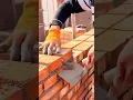 Lagu bricklayer uses a trowel to apply mortar and carefully align red bricks