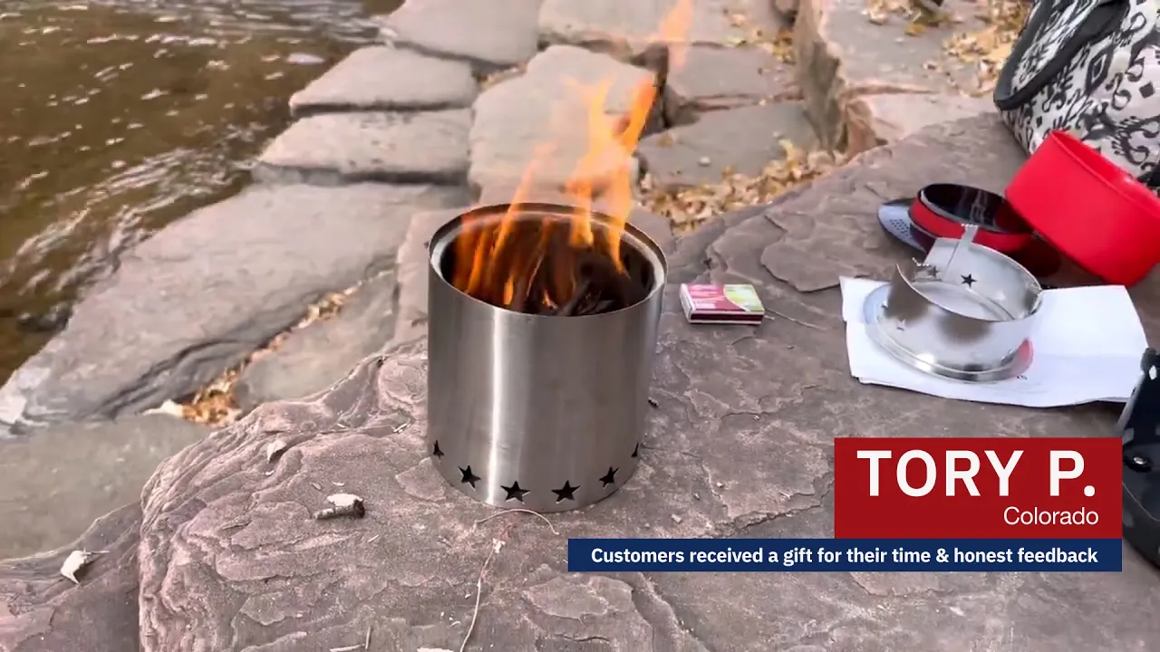 Tory P. from Colorado demonstrates a portable camp stove with a visible flame, set on a rock surface near a river. Nearby are compact cookware pieces, matches, and