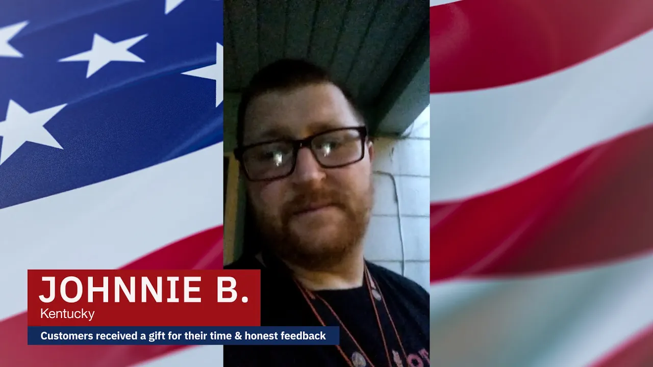 Johnnie B. from Kentucky gives a video testimonial about the 4Patriots BugOUT 2-in-1 Solar Lantern. He stands outside under a covered porch at dusk, wearing glasses and a black shirt, with an American flag-themed background.