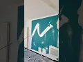 Wall painting in progress featuring a bold white abstract brushstroke over a teal blue background