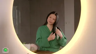 Charming mature Asian woman combing long brown hair with brush in bathroom