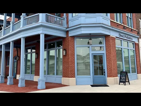 The brick corner of the office building, with pale blue columns, a porch above, and a sidewalk sign by the door.